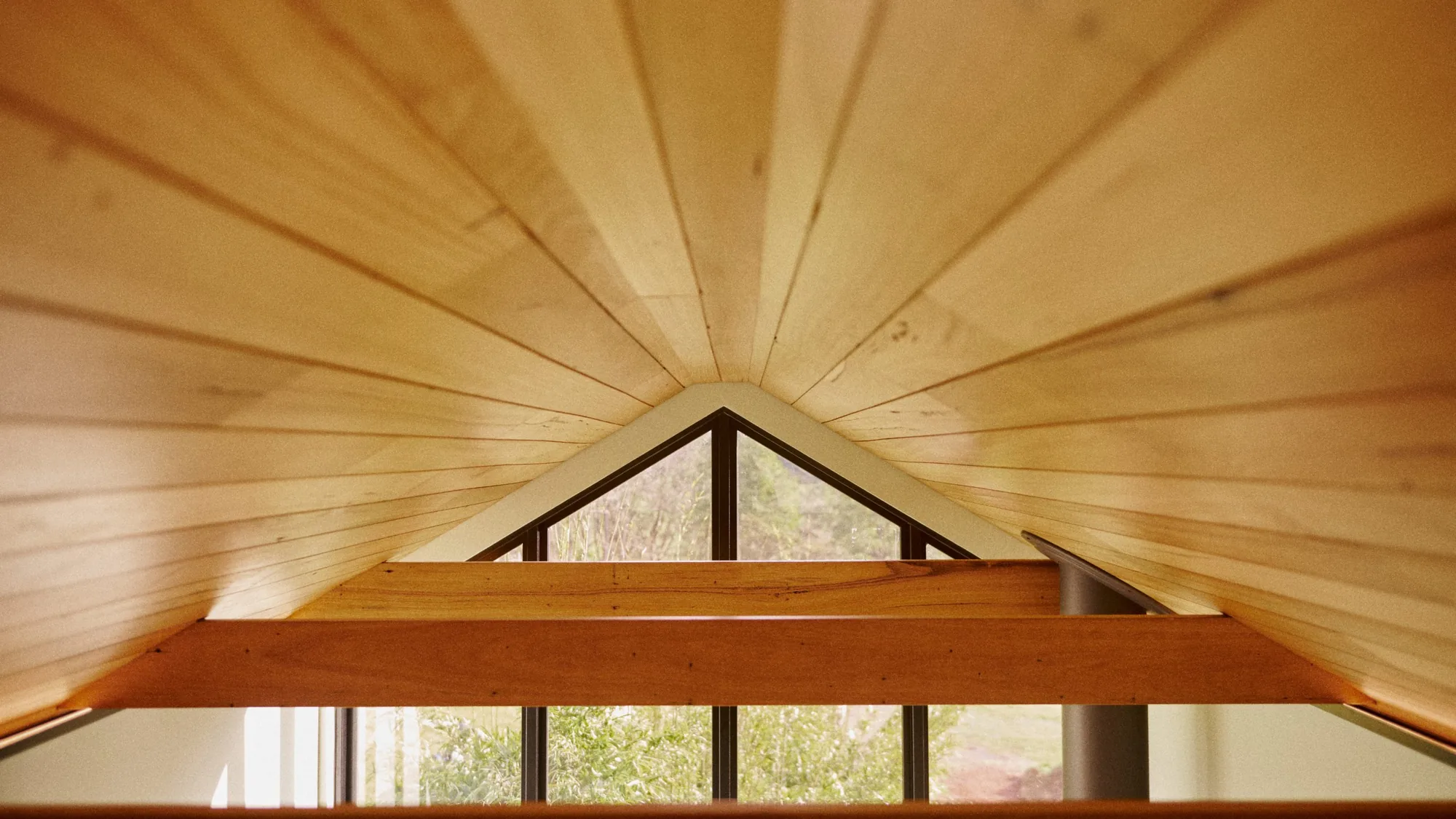 Timber-lined gable ceiling and exposed beams framing a raked window to the garden, built by Amity