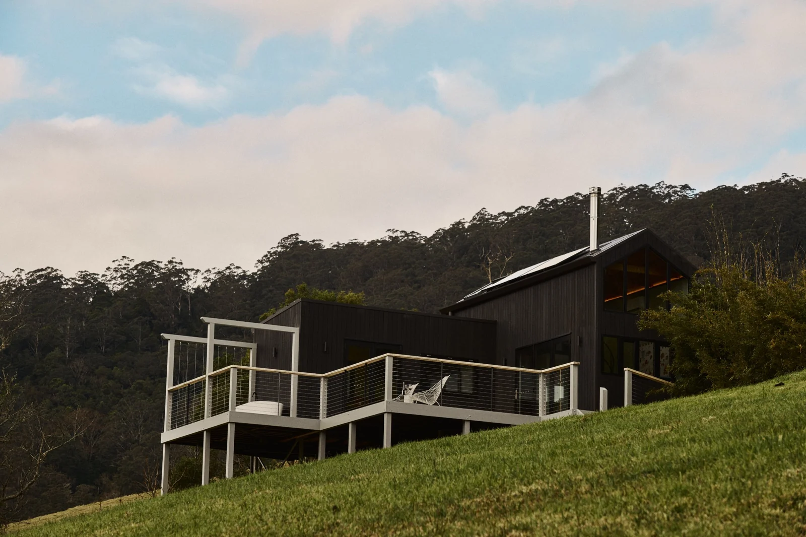 Silent Echo Cabin in Kangaroo Valley, a charcoal-black cabin with a raked gable window and a deck on the slope